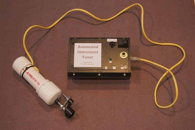 Exterior of device. The black box in the center of the image contains the processing unit of the tuner and the white PVC pipe on the left is the hand-held unit which is placed over the tuning pegs of an instrument.
